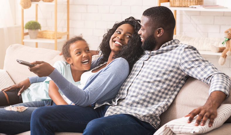 iStock-1184417355-788×462-M-XS Parents sitting on the couch with their daughter and laughing all together